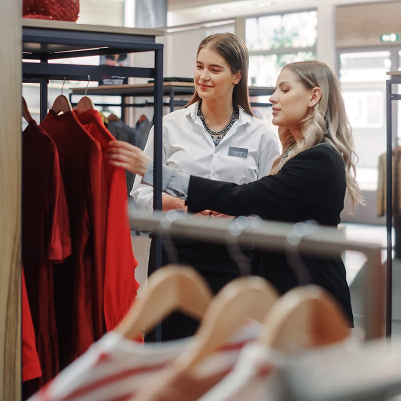 Two female store employees discussing a red garment hanging in the store.